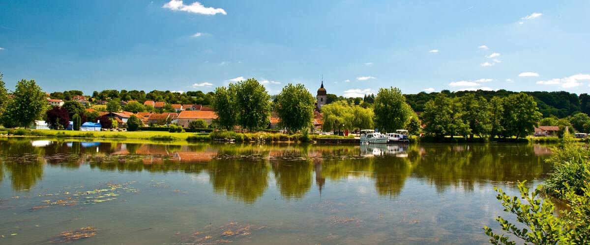 A calm lake with reflections, a church, and houses in the background.