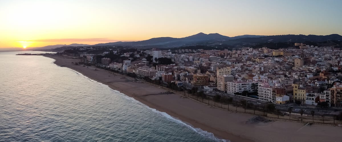 A coastal cityscape at sunset with a beach and buildings along the shore.