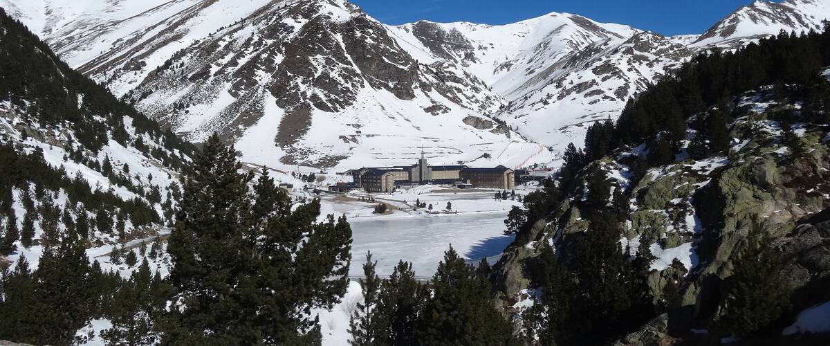 Una cadena montañosa nevada con una estación de esquí y un lago congelado en el valle.