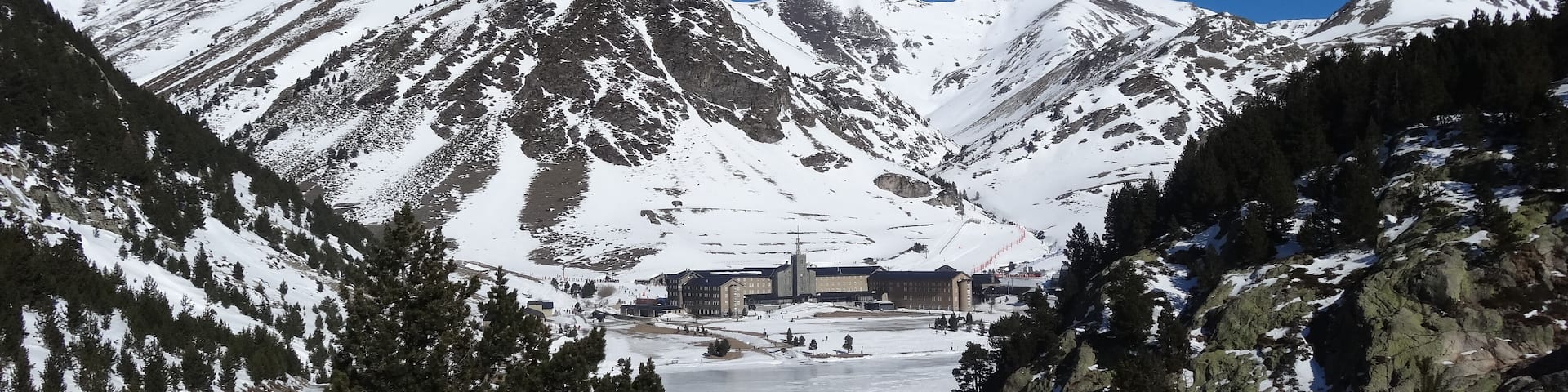 A snow-covered mountain range with a ski resort and a frozen lake in the valley.