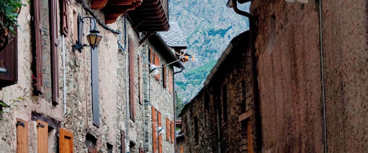 A narrow cobblestone street flanked by rustic stone buildings with wooden shutters and balconies.