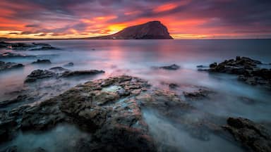 Litoral rochoso ao pôr do sol, com uma colina imponente ao fundo.