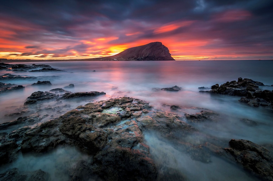 Costa rocosa al atardecer, con una colina destacada al fondo.