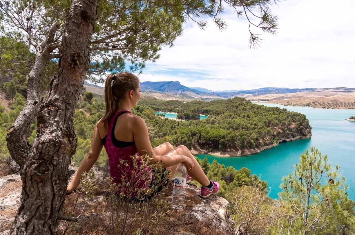 A person sitting on a rock overlooking a turquoise lake surrounded by greenery and mountains.