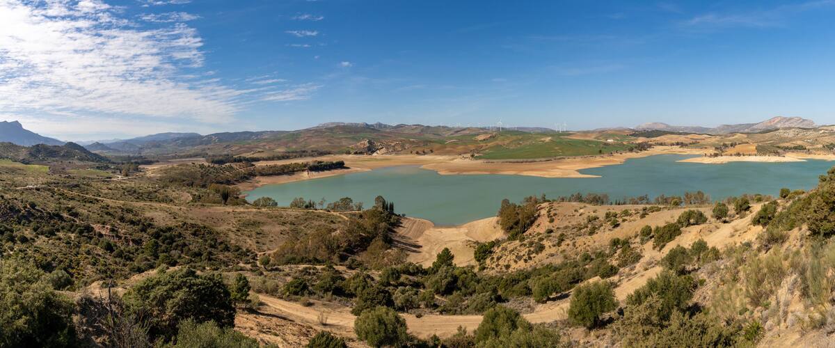 A lake surrounded by hills and wind turbines.