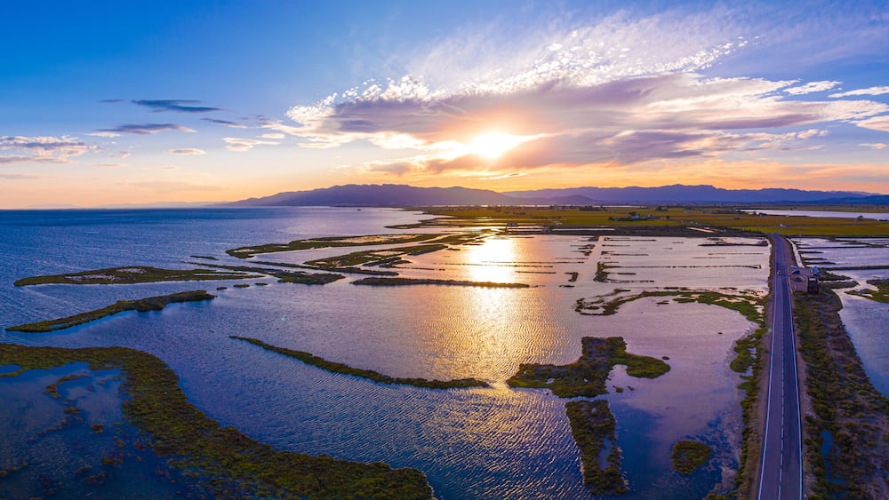 Un paysage côtier avec une route, des étendues d’eau et un coucher de soleil.