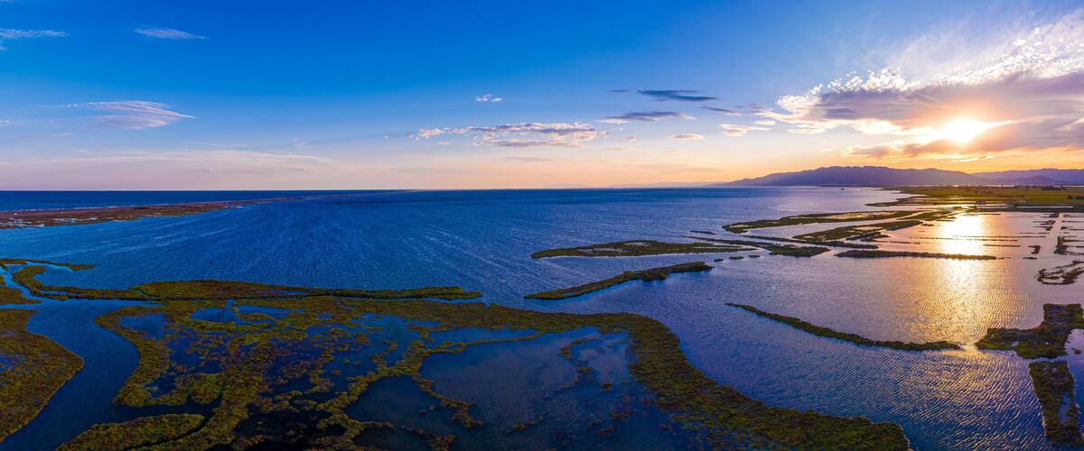 A coastal landscape with a road, water bodies, and a sunset.