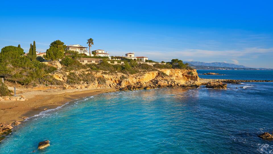 A coastal landscape with clear blue waters, rocky cliffs, and buildings on the hillside.