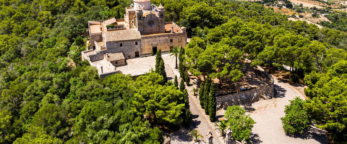 An ancient church surrounded by dense forest and a panoramic view of a valley.