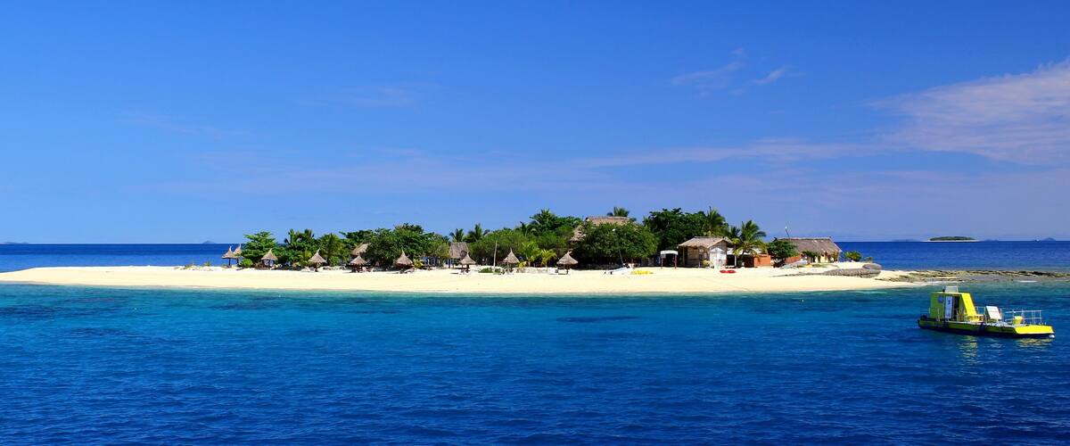 Winzige traumhafte Insel im Pazifik / Hütten und Boot / blaues Meer und klarer Himmel / Fiji