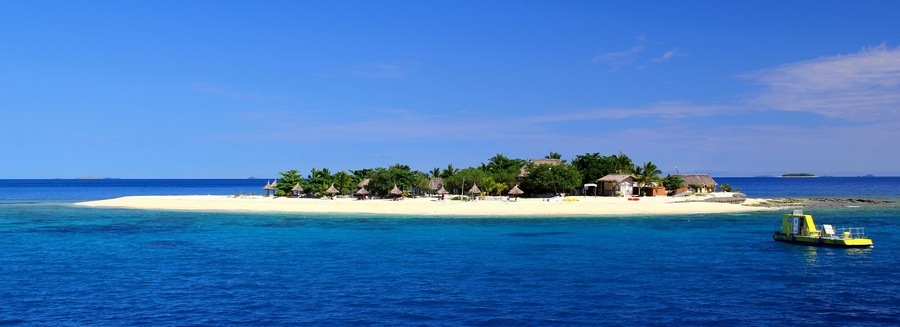 Winzige traumhafte Insel im Pazifik / Hütten und Boot / blaues Meer und klarer Himmel / Fiji