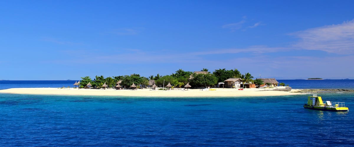 A tropical island with a white sandy beach, palm trees, and a small boat in the water.