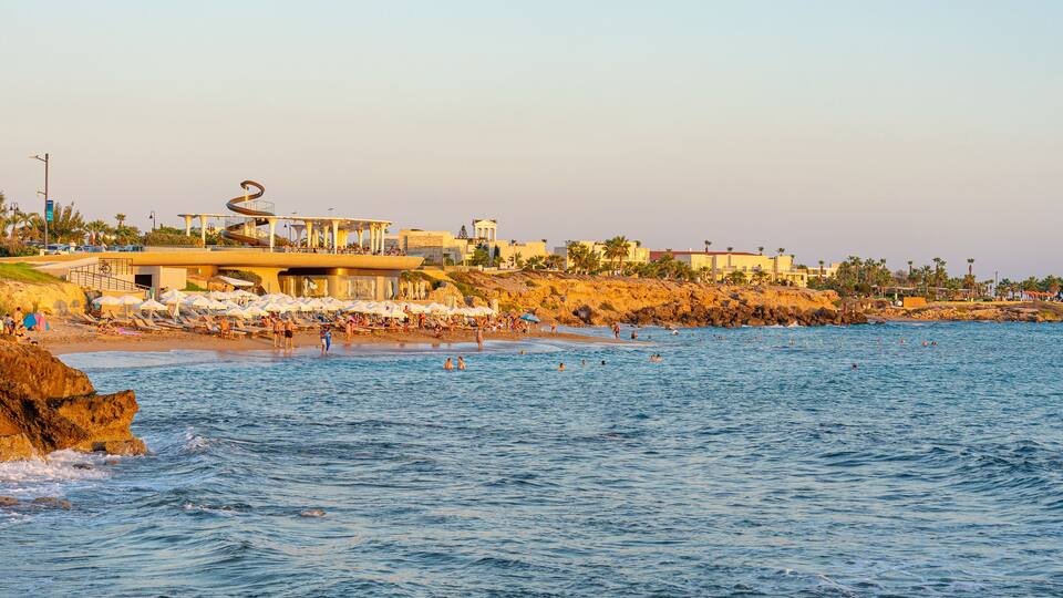 A coastal area with a rocky shoreline, beach umbrellas, and people swimming in the water.
