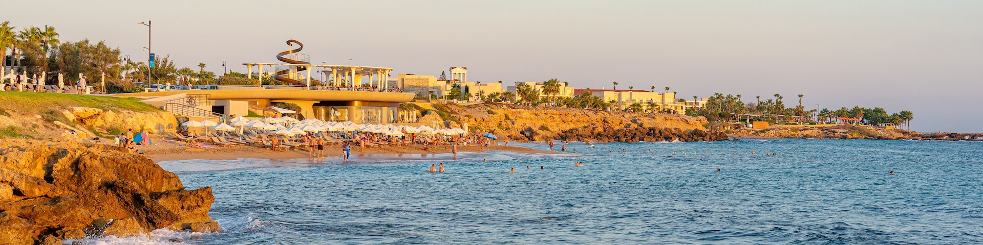 A coastal area with a rocky shoreline, beach umbrellas, and people swimming in the water.