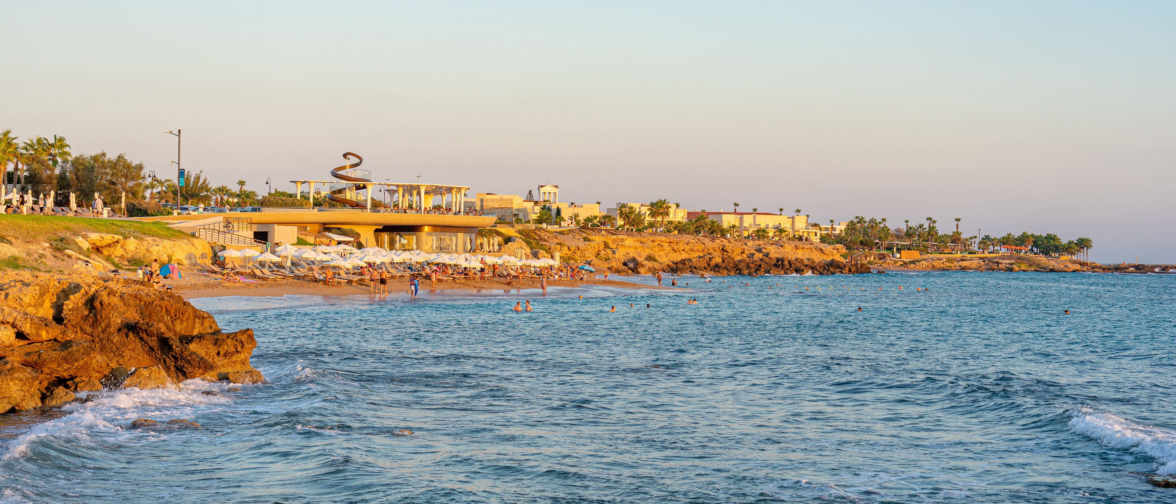 A coastal area with a rocky shoreline, beach umbrellas, and people swimming in the water.
