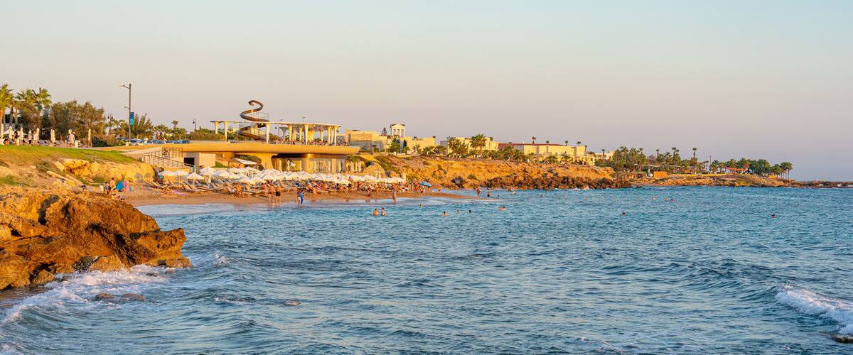 A coastal area with a rocky shoreline, beach umbrellas, and people swimming in the water.