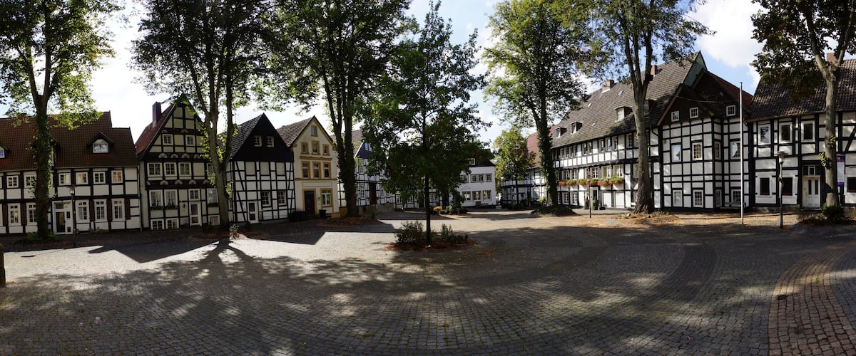 A cobblestone square with traditional half-timbered houses and trees.