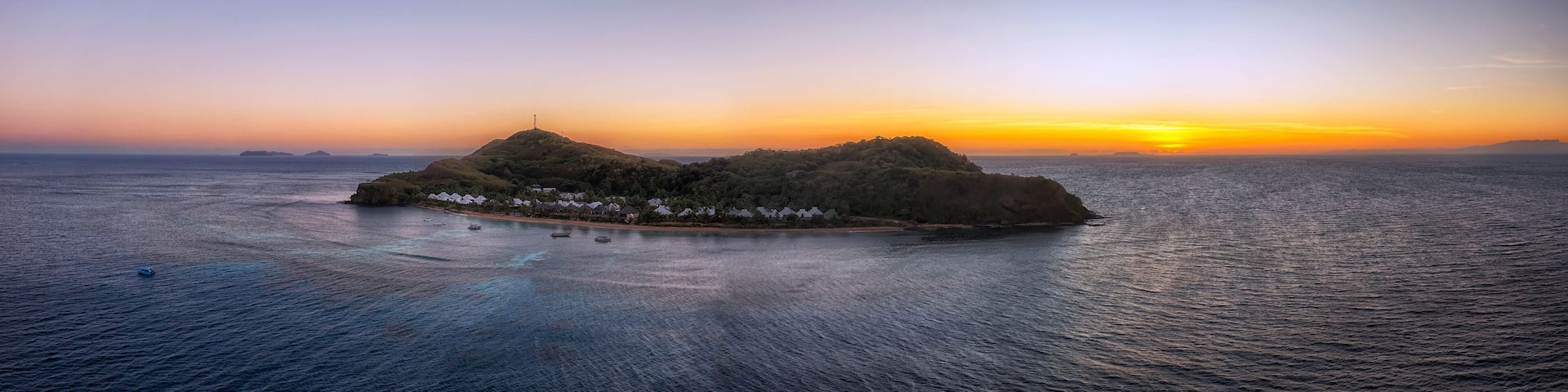 A tropical island with a small settlement at sunset.
