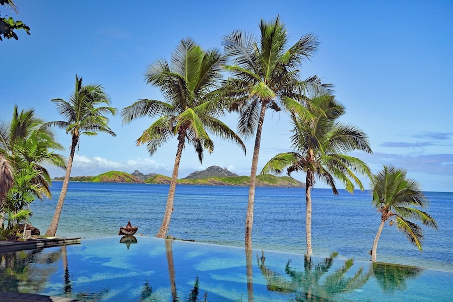 Una piscina infinita tropical con palmeras y un mar azul cristalino.