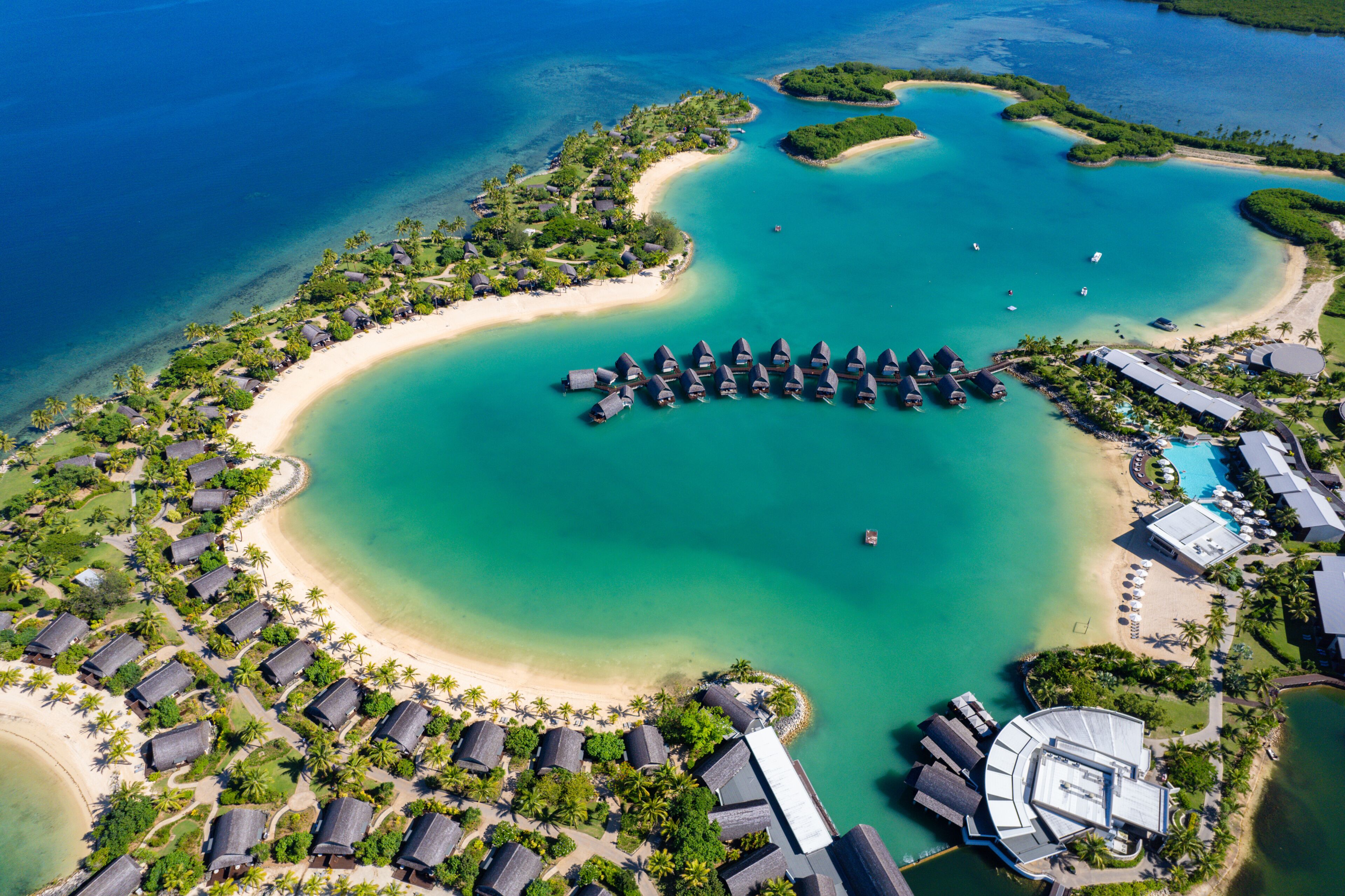 An aerial view of a resort with overwater bungalows, a beach, and clear turquoise waters.