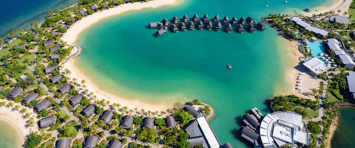 An aerial view of a resort with overwater bungalows, a beach, and clear turquoise waters.