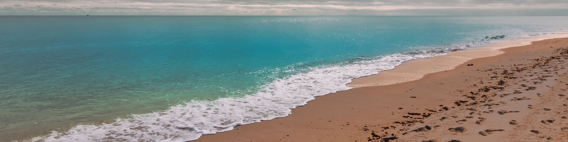 A beach with clear turquoise water, a sandy shore, and footprints.