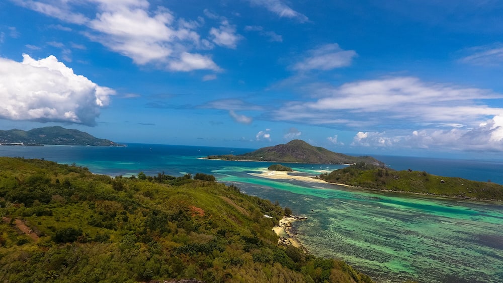 Un paysage insulaire tropical caractérisé par des eaux turquoise cristallines, une végétation luxuriante et un arrière-plan montagneux.