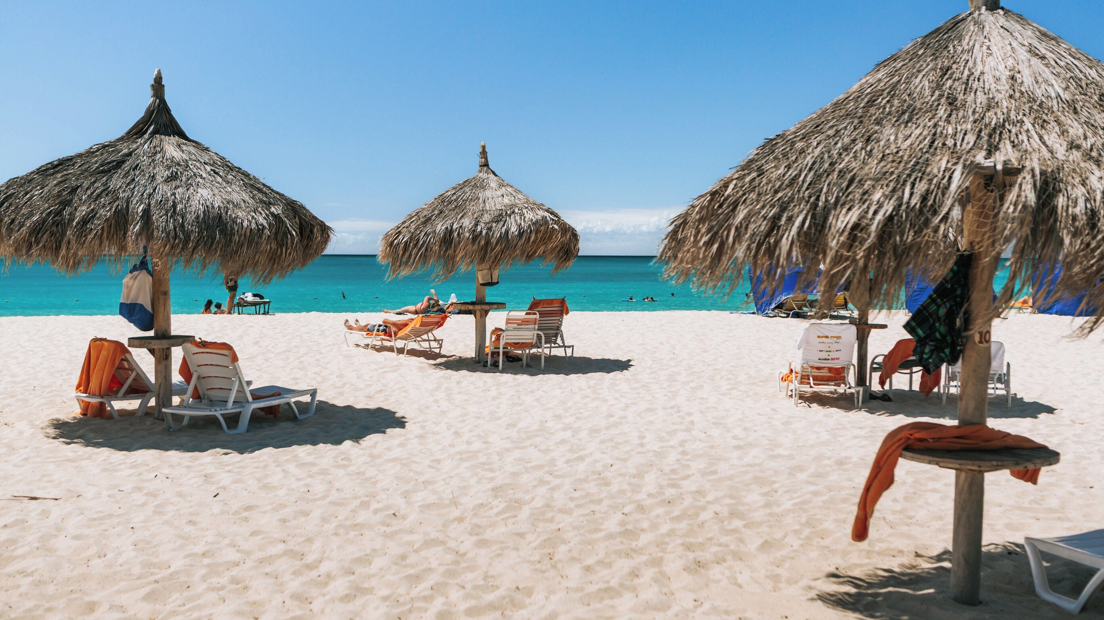 Enjoying the sun at Eagle Beach on a vibrant day in Oranjestad, Aruba with thatched umbrellas providing shade and relaxation by the shimmering sea