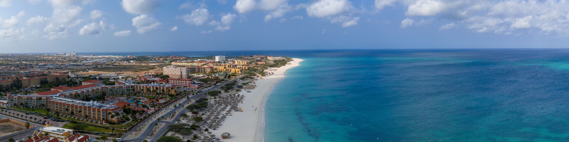 A coastal city with a long sandy beach, clear turquoise waters, and a mix of urban and resort buildings.