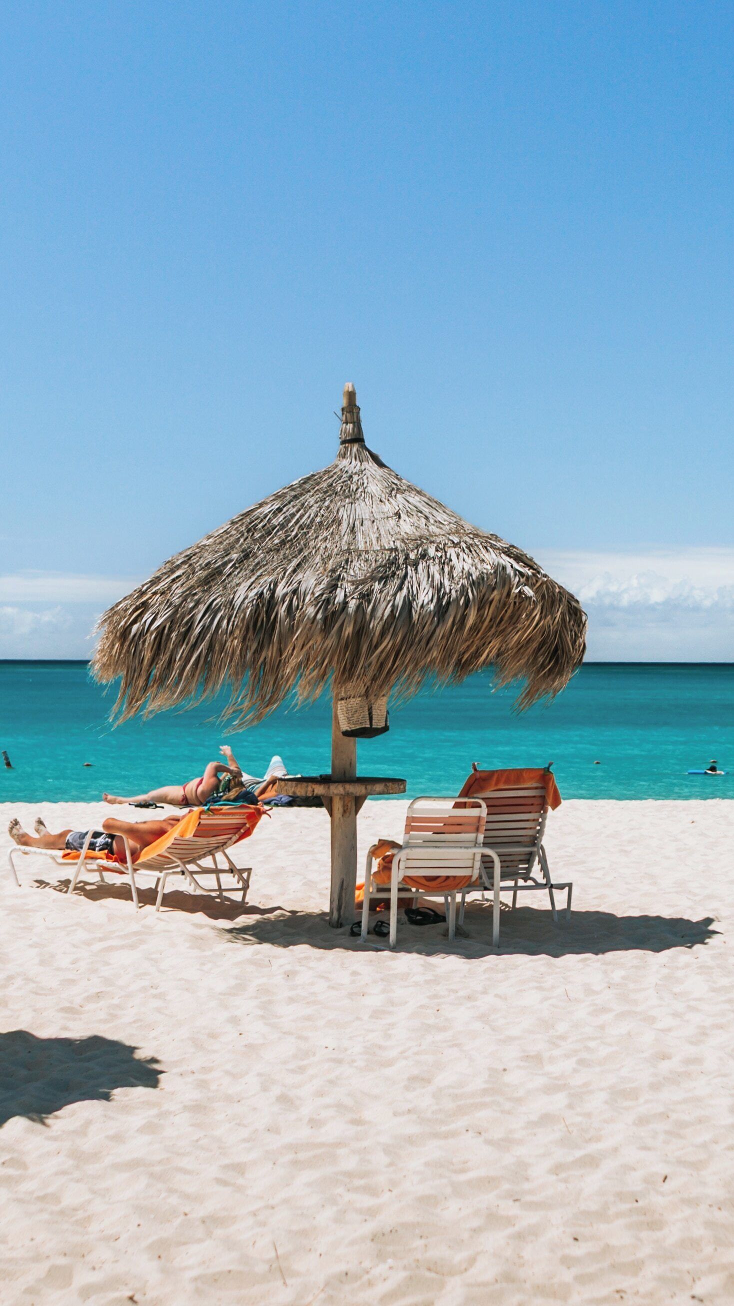 Relaxing under a straw hut at Eagle Beach in Oranjestad, Aruba on a sunny day with crystal-clear waters and soft sand
