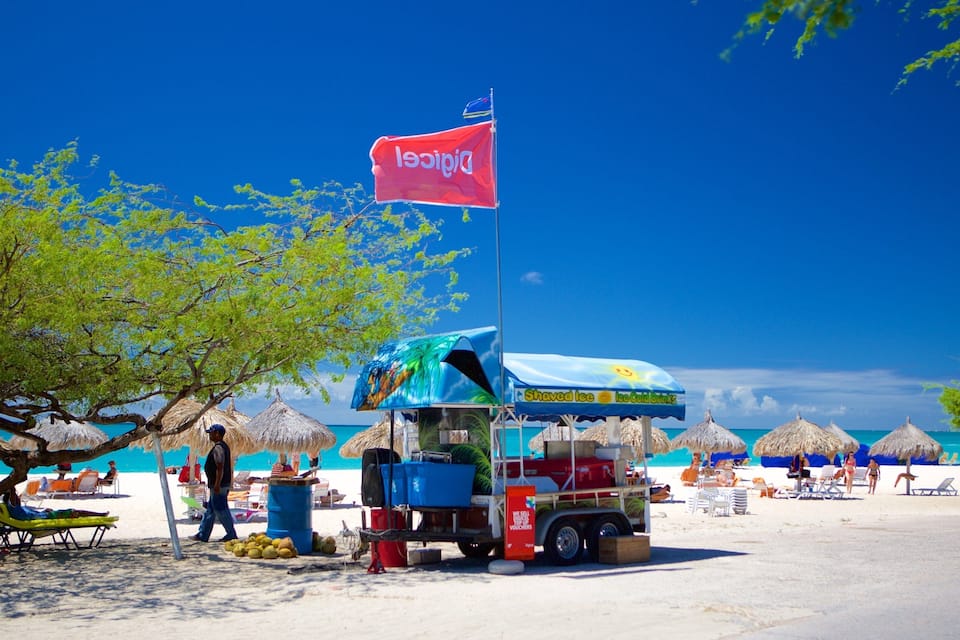 Eine Strandansicht mit einer Flagge, Liegestühlen, Sonnenschirmen und einem Verkaufsstand.