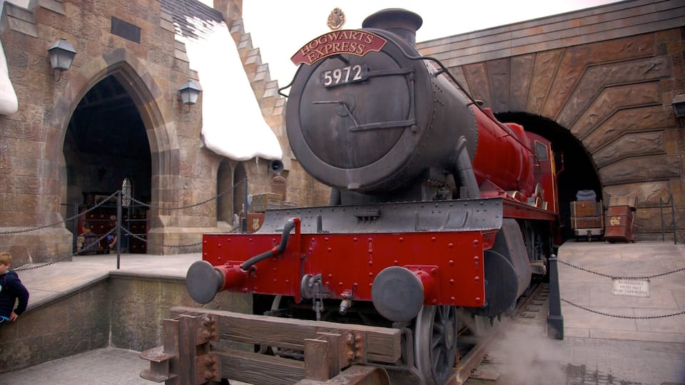 Platform view of a red steam train in front of a themed entrance at Universal Studios Florida during a sunny day