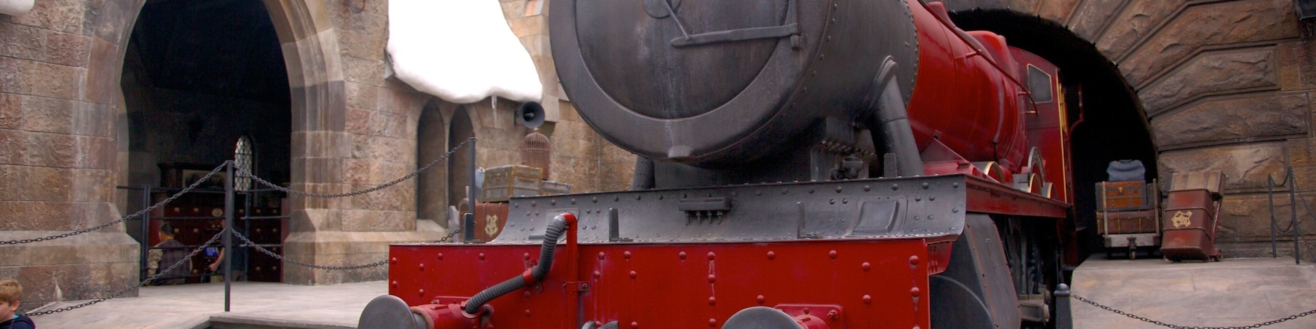Platform view of a red steam train in front of a themed entrance at Universal Studios Florida during a sunny day