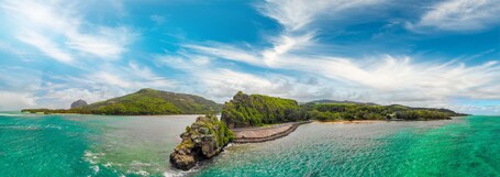 Ein türkisfarbenes Meer, ein felsiger Ausläufer und eine üppig grüne Insel mit einem Berg im Hintergrund.