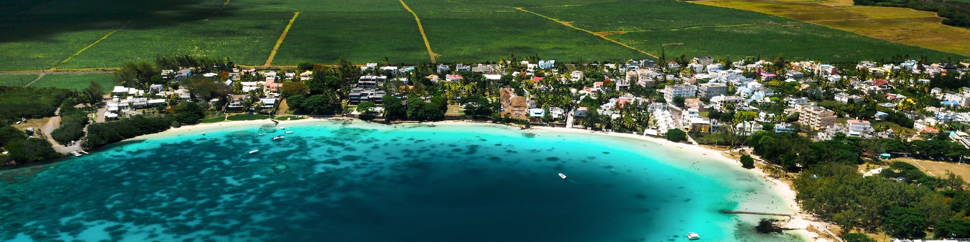 An aerial view of a coastal town with a large bay, clear turquoise waters, and a beach.
