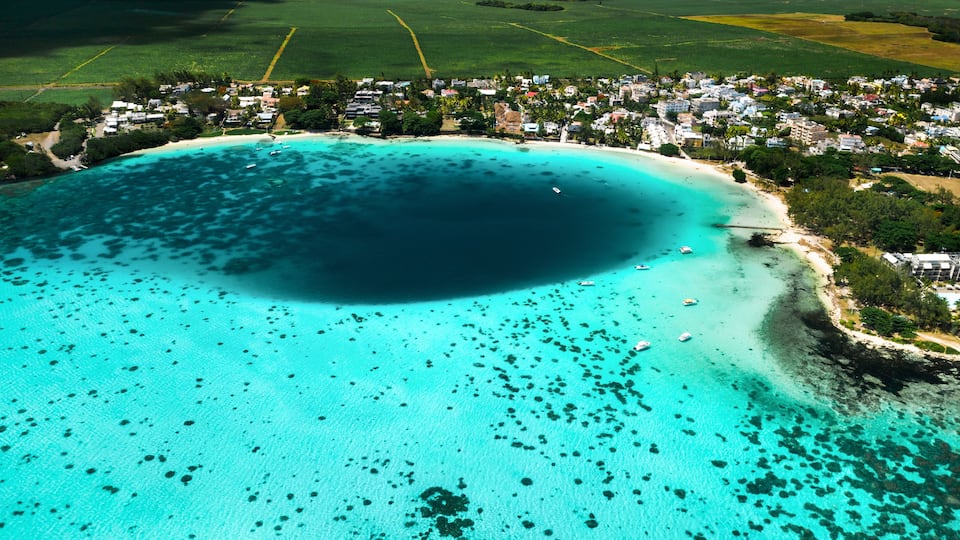 An aerial view of a coastal town with a large bay, clear turquoise waters, and a beach.