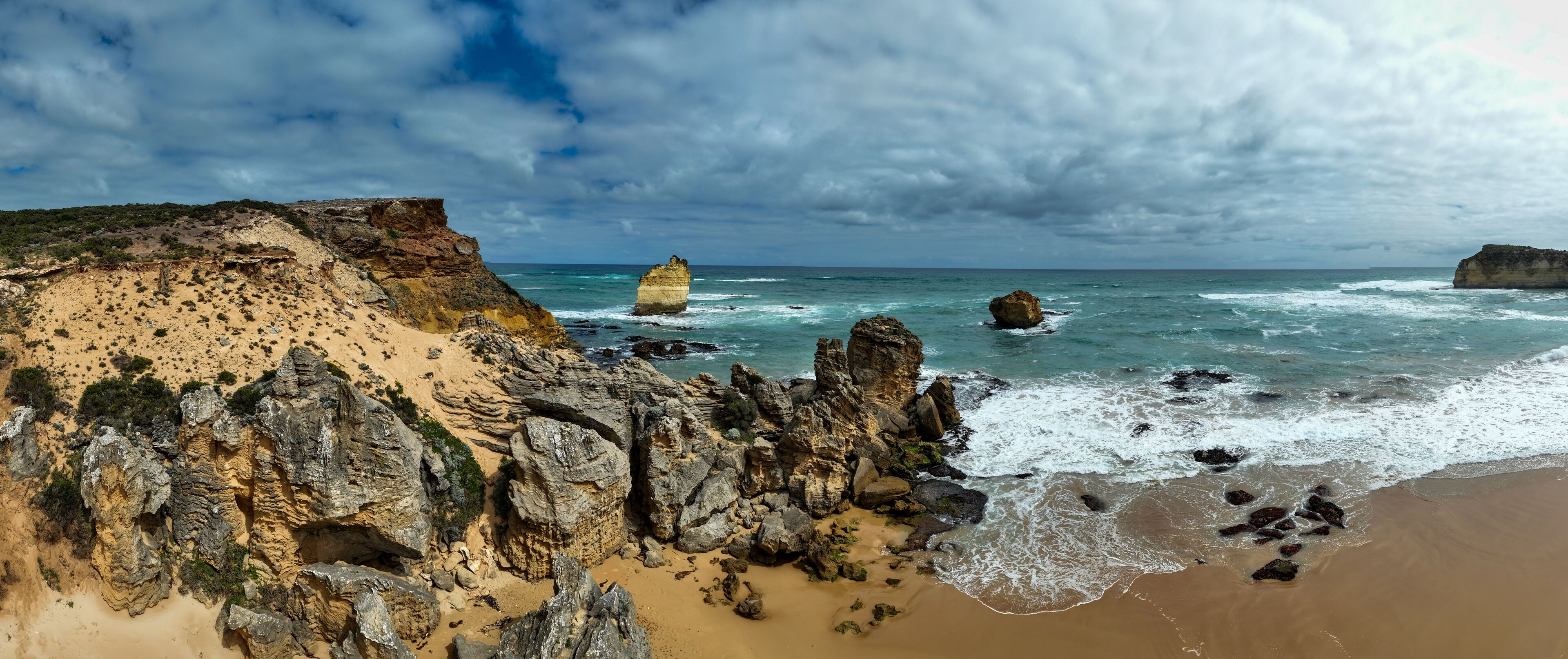 A coastal landscape with rocky cliffs, sandy beach, and the ocean.