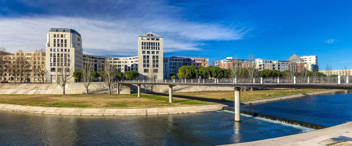 A river with a bridge, modern buildings, and a clear blue sky.