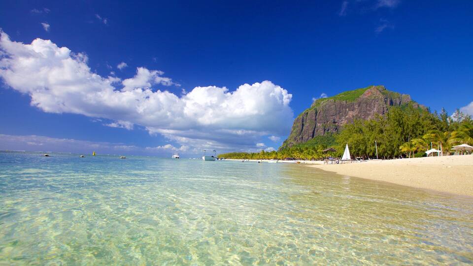 A clear blue sea, a sandy beach, and a large mountain.
