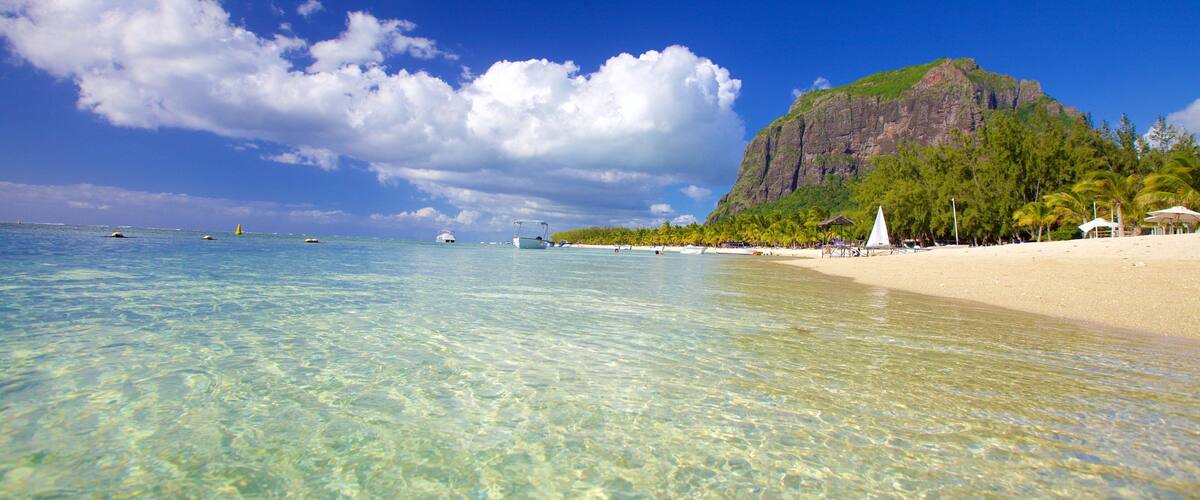 A clear blue sea, a sandy beach, and a large mountain.