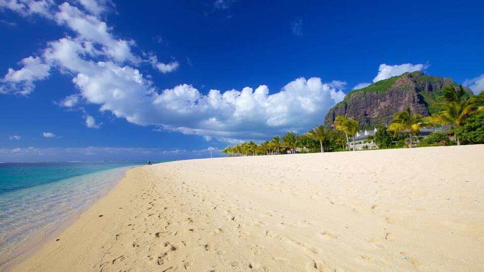A beach with clear turquoise water, a sandy shore, and a mountain in the background.