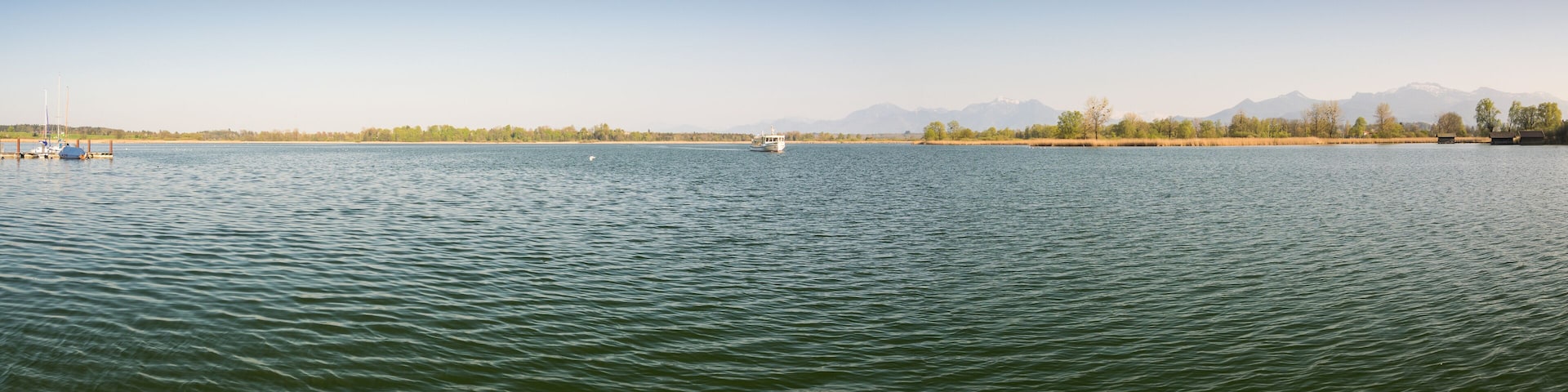 A calm lake with a boat, distant mountains, and a clear sky.