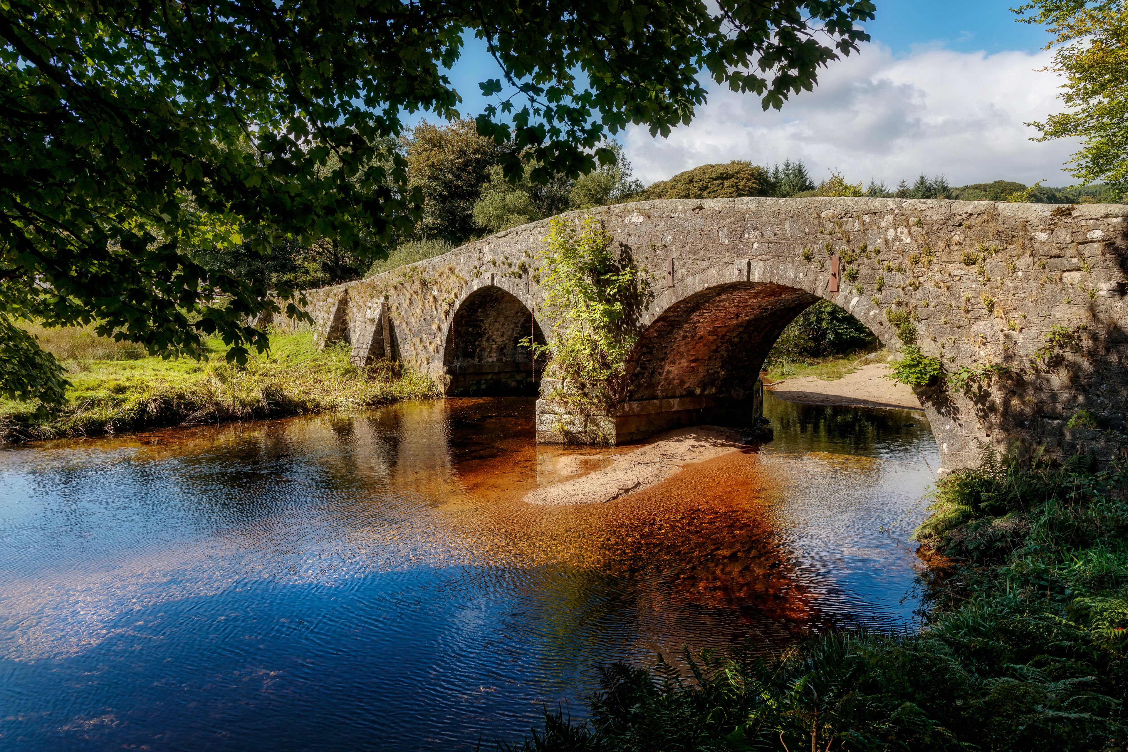 A stone bridge over a river with arches, surrounded by greenery and trees.