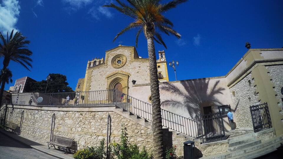 A historic church with a clock tower, palm trees, and a stone wall.