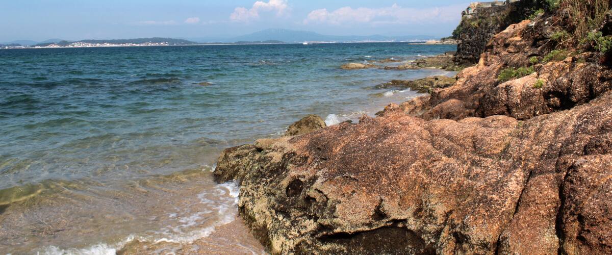A rocky coastline with clear blue water and distant mountains.