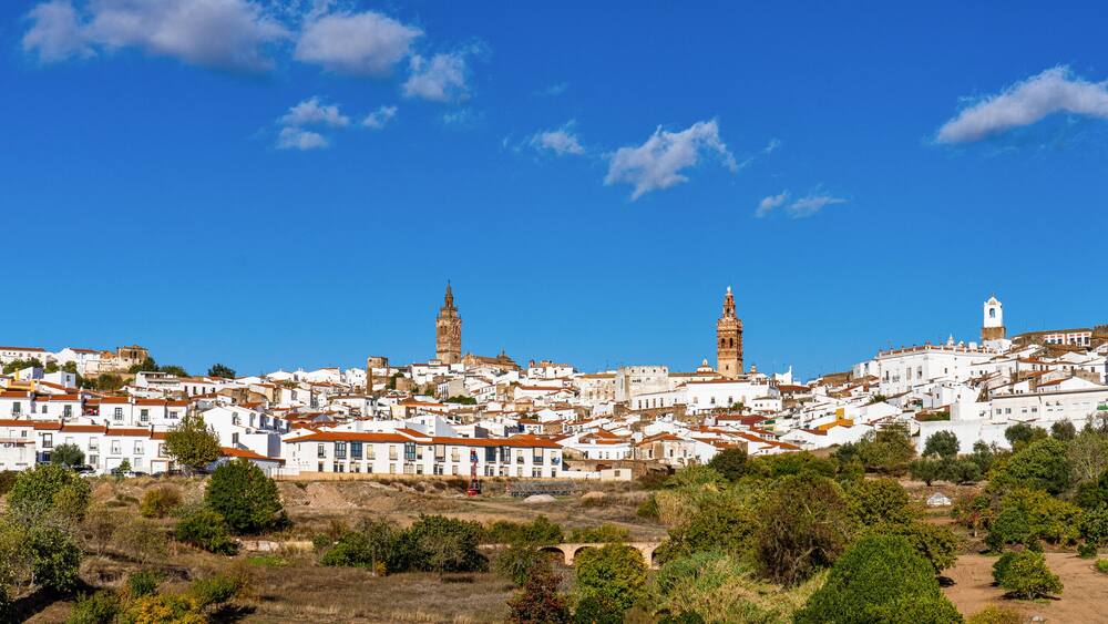 A coastal town with white buildings, a prominent church tower, and a sea view.