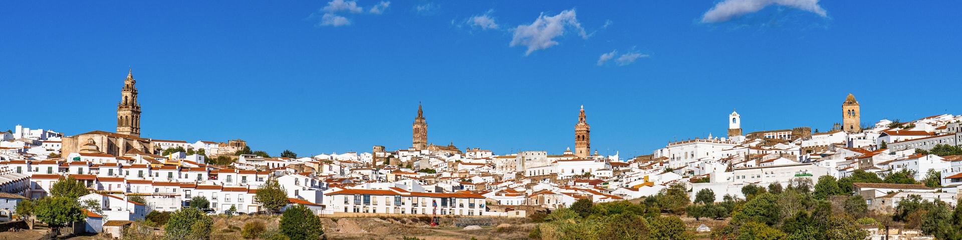 Un pueblo costero con edificios blancos, una torre de iglesia destacada y vistas al mar.