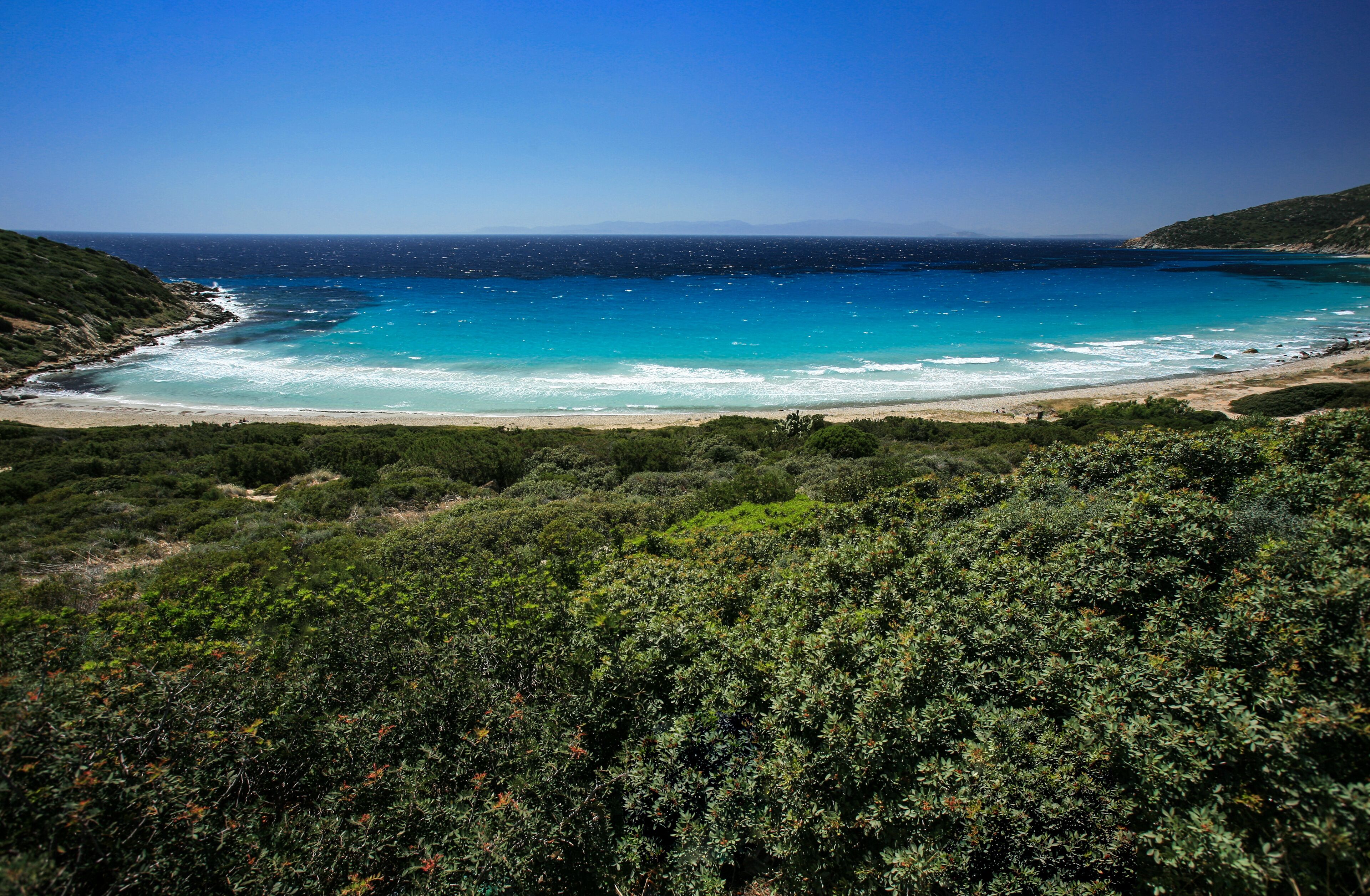 A coastal landscape with a beach, turquoise sea, and dense greenery.