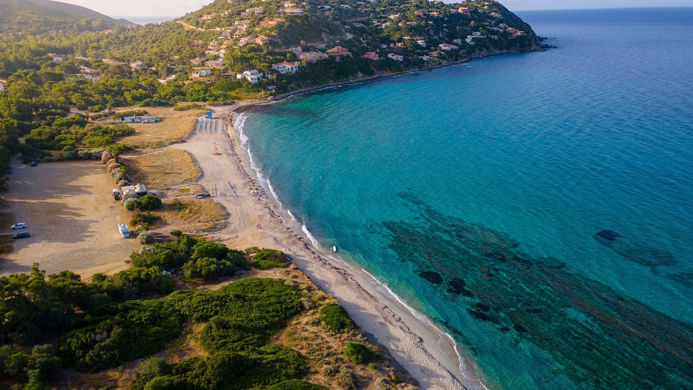 A coastal landscape with a beach, clear turquoise waters, and a hillside settlement.