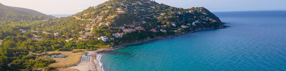 A coastal landscape with a beach, clear turquoise waters, and a hillside settlement.
